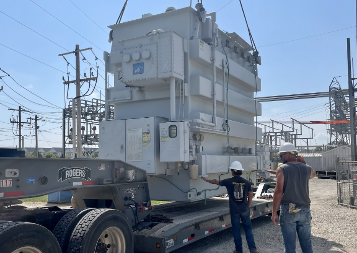 Two men from MCF Waukesha Industrials Rigging loading a large transformer onto a truck.