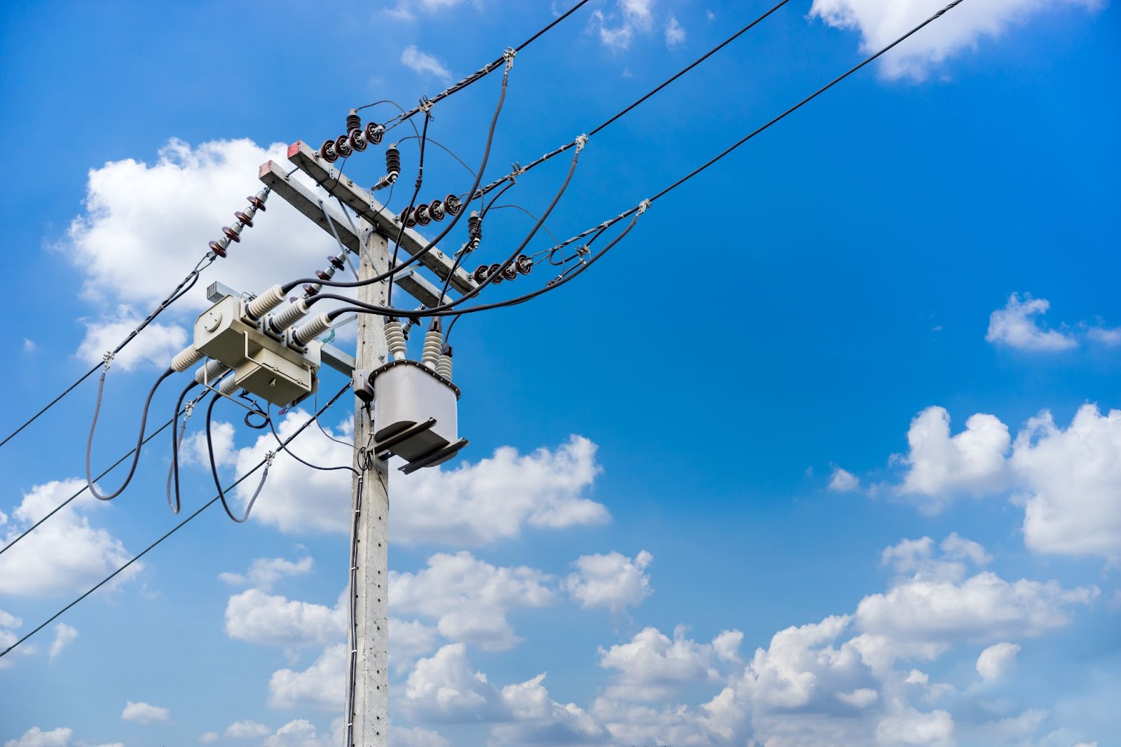 Utility pole with a transformer and wires against a cloudy blue sky.