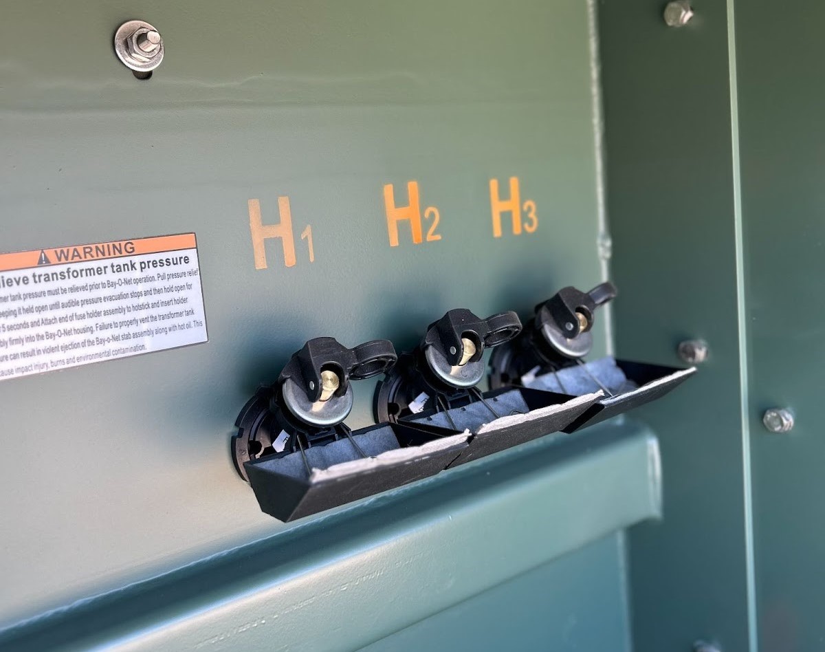 Close-up of a green electrical transformer panel with labeled terminals(H1,H2, H3)and warning label.