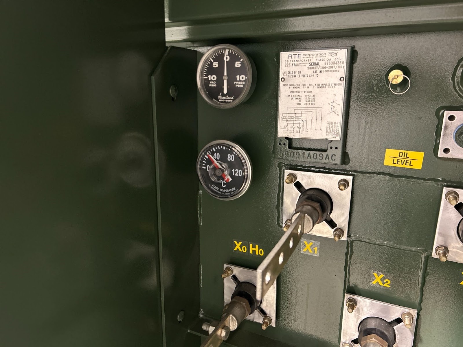 Close-up of a green transformer panel with gauges showing oil pressure and liquid temperaturelabeled with RTE Corporation details and connection points Xo Ho X1 and X2