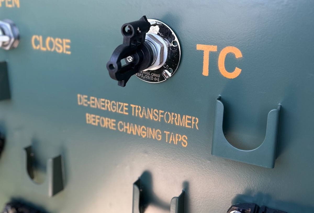 Green electrical panel with OPENCLOSE switch and DE-ENERGIZE TRANSFORMER BEFORE CHANGING TAPS label.