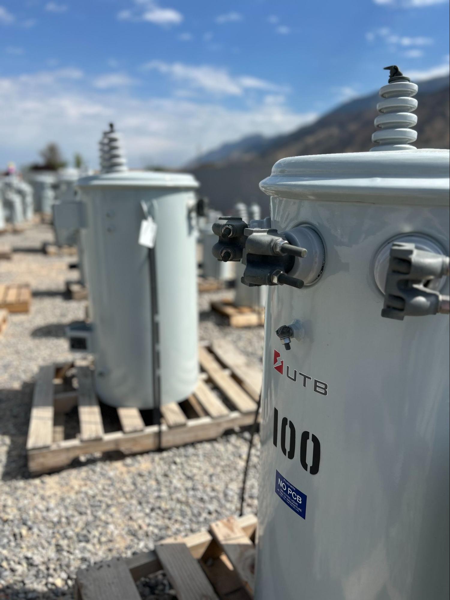 UTB distribution transformers on pallets with mountain backdrop.
