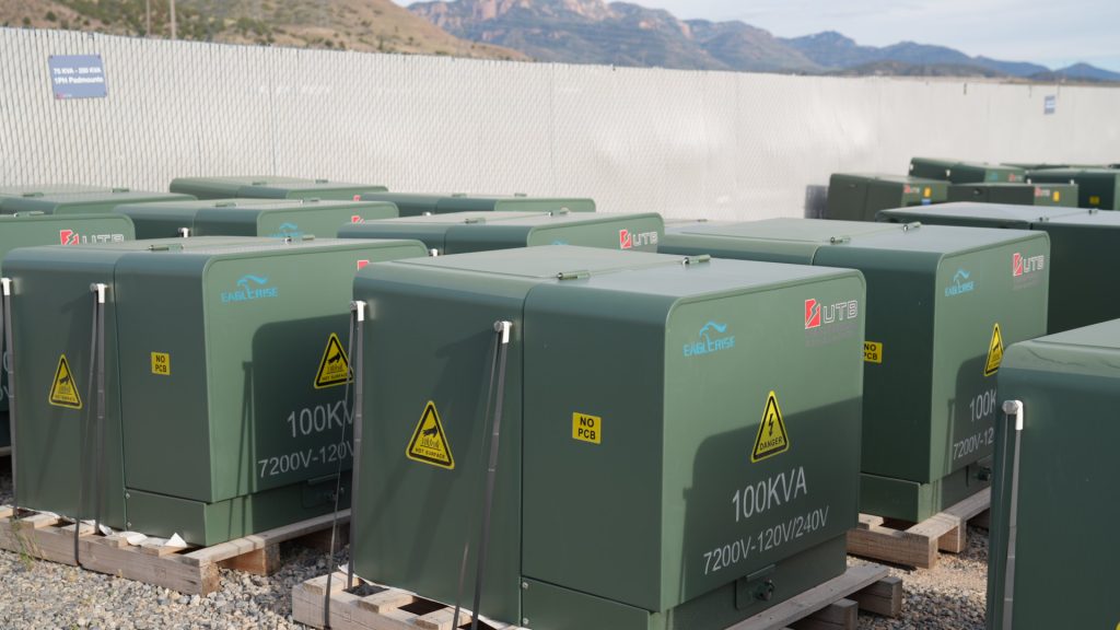 Green pad-mounted electrical transformers lined up in the UTB Transformers yard.